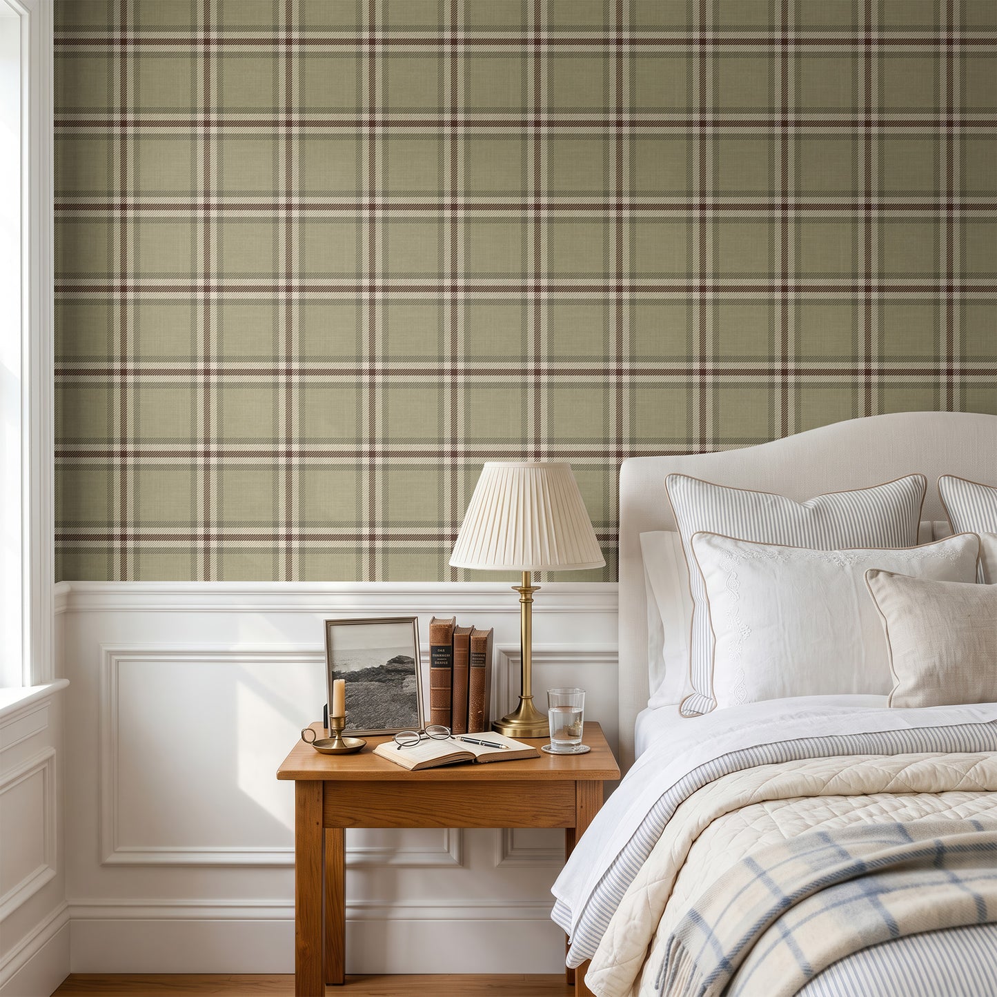 A styled bedroom interior featuring a sage green and beige plaid wallpaper on the upper wall, white wainscoting below, a wooden nightstand with a lamp and books, and a neatly made bed with white linens and a plaid throw blanket.