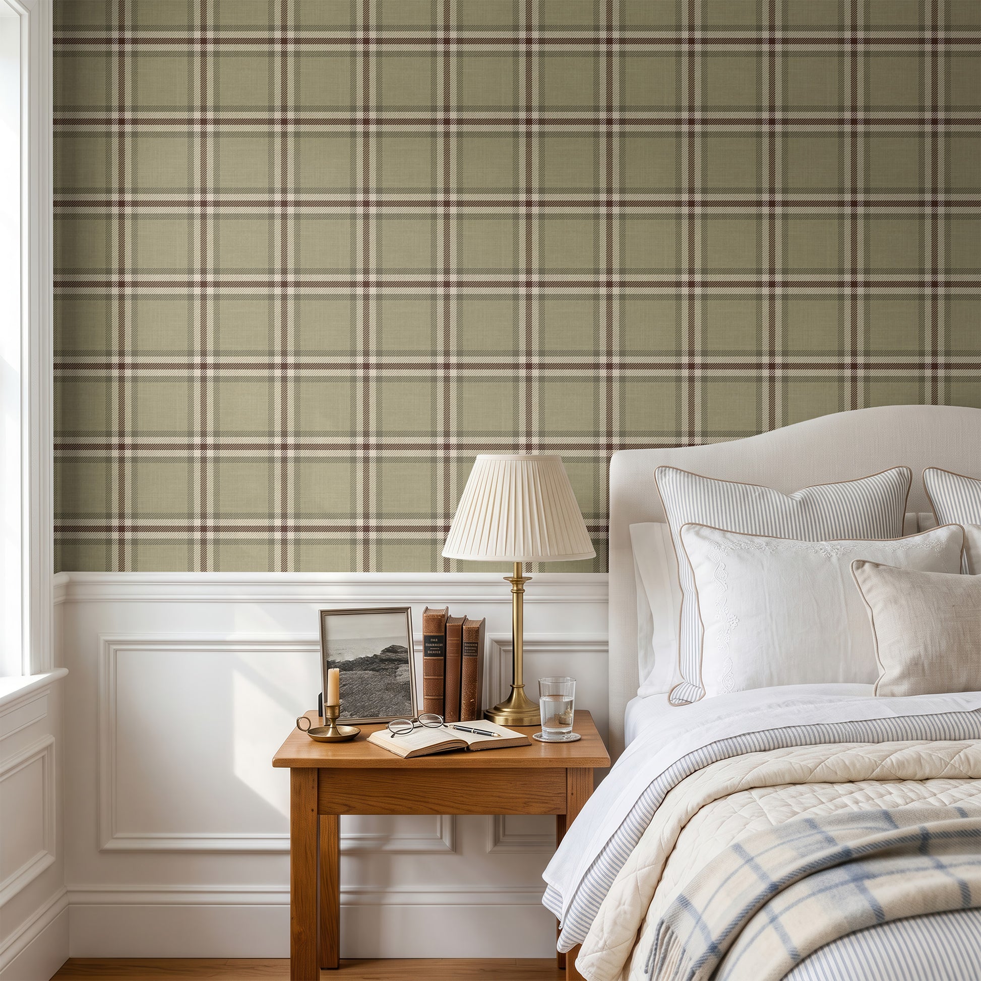 A styled bedroom interior featuring a sage green and beige plaid wallpaper on the upper wall, white wainscoting below, a wooden nightstand with a lamp and books, and a neatly made bed with white linens and a plaid throw blanket.