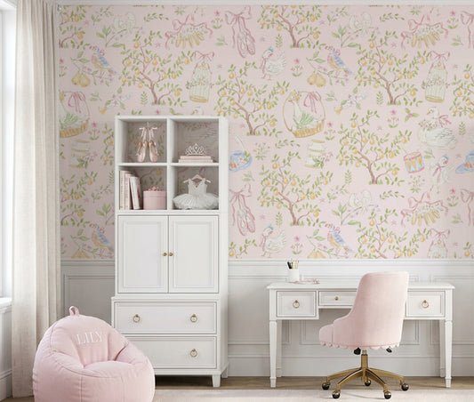 A styled children's room featuring light pink wallpaper with a whimsical tree and bird pattern, a white cabinet, a white desk with a pink chair, and a pink beanbag chair.