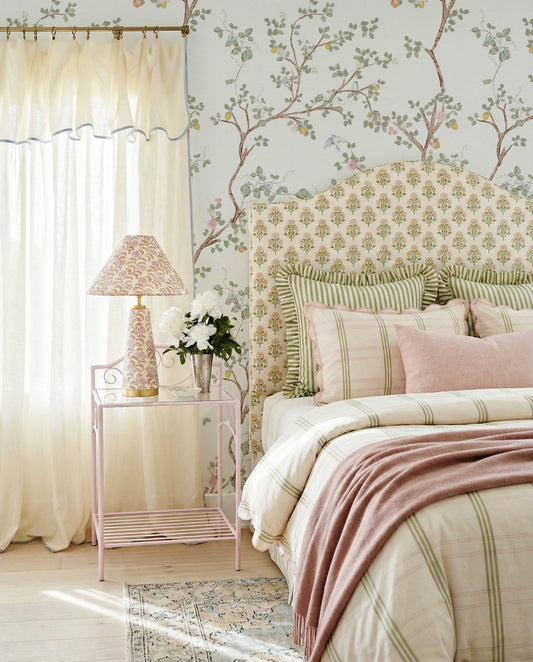 Cozy bedroom with Chinoiserie floral wallpaper, bed with striped bedding, and side table with lamp.